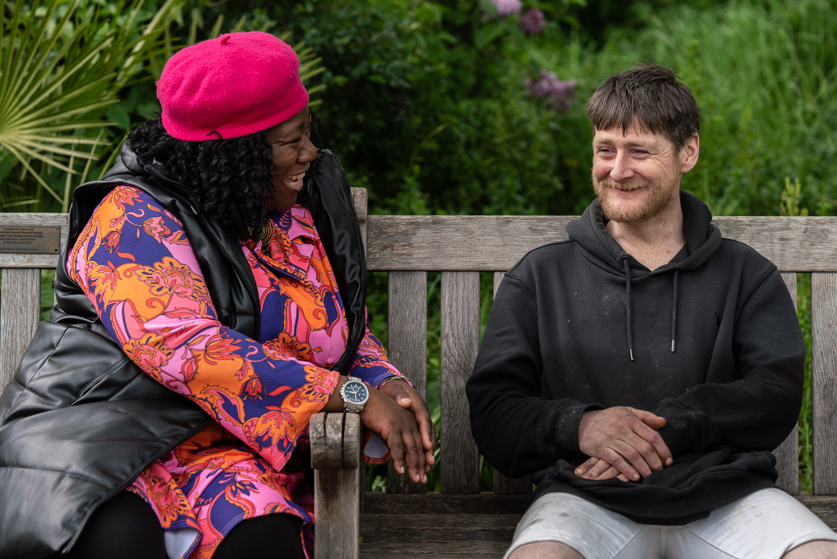 A support worker sits on a park bench and chats with a Look Ahead customer who has experienced homelessness.